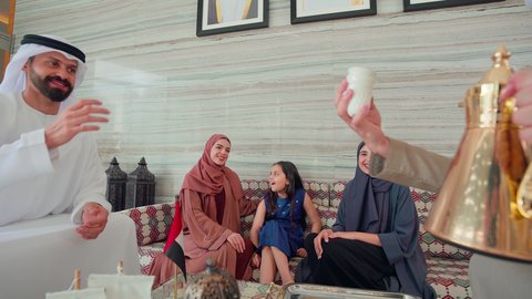 ايماءات البشاشة والترحيب بالضيوف ، مفهوم الضيافة والاستقبال , تقديم القهوة العربية ,  قضاء اوقات سعيده مع العائلة ، رجل عربي اماراتي خليجي يرتدي الكندورة والغتره يقوم بصب القهوه من الدله النحاسية