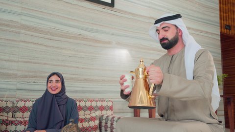مفهوم الضيافة والاستقبال , تقديم القهوة العربية ,  قضاء اوقات سعيده مع العائلة ، رجل عربي اماراتي خليجي يرتدي الكندورة والغتره يقوم بصب القهوه من الدله النحاسية ,  ايماءات البشاشة والترحيب بالضيوف