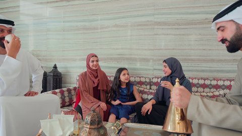 قضاء اوقات سعيده مع العائلة ، رجل عربي اماراتي خليجي يرتدي الكندورة والغتره يقوم بصب القهوه من الدله النحاسية , تقديم القهوة العربية , مفهوم الضيافة والاستقبال , ايماءات البشاشة والترحيب بالضيوف