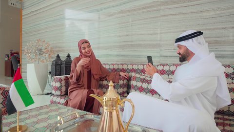 كافيهات ومقاهي بالامارات، توثيق اللحظات التذكارية عبر الجوال ،رجل عربي خليجي اماراتي يرتدي الكندورة والغتره يقوم بالتقاط صورة لزوجته ،ايماءات السرور والسعاده ،  قضاء اوقات سعيده