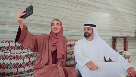 التقاط صور السيلفي ، توثيق اللحظات التذكارية عبر الجوال ،زوجان عربيان خليجيان اماراتيان يجلسان فى المقهي،ايماءات السرور والسعاده ، كافيهات ومقاهي بالامارات، قضاء اوقات سعيده