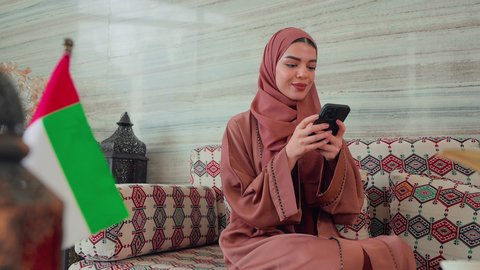 كافيهات ومقاهي الامارات، توثيق اللحظات التذكاريه ، اجراء مكالمه هاتفيه باستخدام الجوال ،  الاطمئنان على الاهل والاصدقاء، نزهه فى الخارج ،ايماءات السرور والسعاده ، قضاء اوقات سعيده ، امراه عربيه خليجيه اماراتيه تجلس فى مقهي وبجانبها علم الامارات