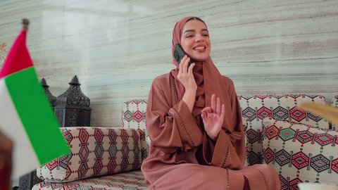 اجراء مكالمه هاتفيه باستخدام الجوال ،  الاطمئنان على الاهل والاصدقاء، نزهه فى الخارج ،ايماءات السرور والسعاده ، قضاء اوقات سعيده ، كافيهات ومقاهي الامارات، توثيق اللحظات التذكاريه ، امراه عربيه خليجيه اماراتيه تجلس فى مقهي وبجانبها علم الامارات