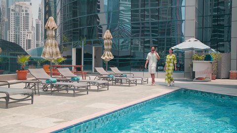 An Arab Gulf Emirati couple in casual wear strolling around the pool at a hotel in Saudi Arabia, luxury chalets and resorts, doing fun recreational activities, breathing fresh air