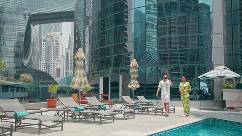 شاليهات و منتجعات فاخرة ، القيام بالأنشطة الترفيهية المسلية,  استنشاق الهواء النقي ،زوجان عربيان خليجيان اماراتيين يرتديان الزي الكاجوال يتجولان حول المسبح في أحد الفنادق في المملكة العربية السعودية