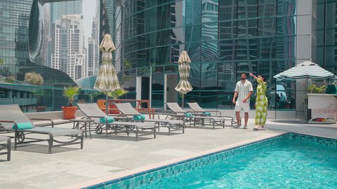 استنشاق الهواء النقي ،القيام بالأنشطة الترفيهية المسلية, زوجان عربيان خليجيان اماراتيين يرتديان الزي الكاجوال يتجولان حول المسبح في أحد الفنادق في المملكة العربية السعودية، شاليهات و منتجعات فاخرة