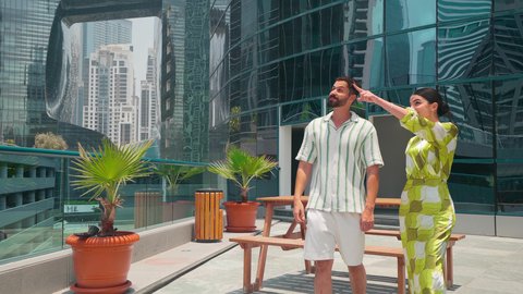 مشاهدة التطور العمراني في المدينة، التجول واستنشاق الهواء النقي في الخارج,النمو العمراني في الامارات ، تحديد موقع معين ،  الفخر والاعتزاز بالتقدم المعماري ، الاطمئنان على الاهل والاصدقاء ،زوجان عربيان خليجيان اماراتيان يرتديان الزي الكاجوال ينظران الي شئ ما