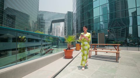 Watching the urban development in the city, walking around and breathing fresh air outside, being proud of the architectural progress, checking on family and friends, urban growth in the Emirates, an Arab Gulf Emirati woman wearing casual clothes using a mobile phone