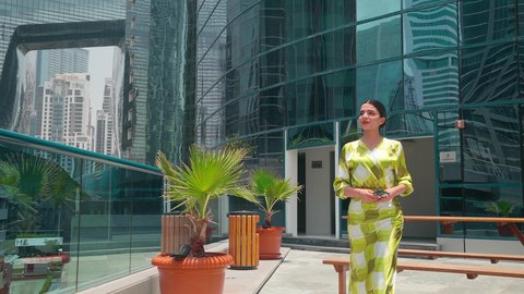 التجول واستنشاق الهواء النقي في الخارج,  الفخر والاعتزاز بالتقدم المعماري ، الاطمئنان على الاهل والاصدقاء ، مشاهدة التطور العمراني في المدينة،النمو العمراني في الامارات ،امراه عربيه خليجيه اماراتيه ترتدي الزي الكاجوال تستخدم الهاتف المحمول