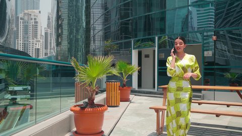 Checking on family and friends, watching the urban development in the city, walking around and breathing fresh air outside, being proud of the architectural progress, chatting online, urban growth in the Emirates, an Arab Gulf Emirati woman wearing casual clothes using a mobile phone