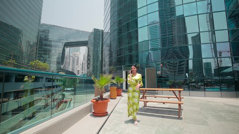 اجراء مكالمه هاتفيه ، مشاهدة التطور العمراني في المدينة، التجول واستنشاق الهواء النقي في الخارج, الفخر والاعتزاز بالتقدم المعماري ، الدردشة عبر الانترنت ، النمو العمراني في الامارات ،امراه عربيه خليجيه اماراتيه ترتدي الزي الكاجوال تستخدم الهاتف المحمول