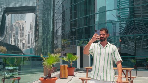 الدردشة عبر الانترنت ، النمو العمراني في الامارات ، الفخر والاعتزاز بالتقدم المعماري ، مشاهدة التطور العمراني في المدينة،  التجول واستنشاق الهواء النقي في الخارج, رجل عربي خليجي اماراتي يرتدي الزي الكاجوال يستخدم الهاتف المحمول