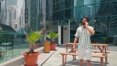 مشاهدة التطور العمراني في المدينة، النمو العمراني في الامارات ، الفخر والاعتزاز بالتقدم المعماري ، التجول واستنشاق الهواء النقي في الخارج, رجل عربي خليجي اماراتي يرتدي الزي الكاجوال يستخدم الهاتف المحمول