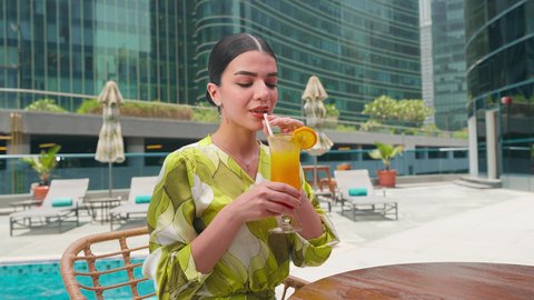 امراه عربيه خليجيه اماراتيه ترتدي الزي الكاجوال تستمتع بالجلوس على طاولة حول المسبح في أحد الفنادق في المملكة العربية السعودية ،  قضاء اوقات سعيدة ، الاستمتاع بالمشروبات الصيفية المنعشة ، شاليهات و منتجعات فاخرة، القيام بالأنشطة الترفيهية المسلية