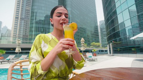 Having a good time, enjoying refreshing summer drinks, luxury chalets and resorts, doing fun recreational activities, an Emirati Gulf Arab woman wearing casual clothes enjoying sitting at a table around the pool in a hotel in the Kingdom of Saudi Arabia
