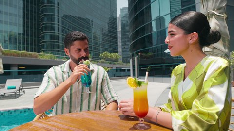 Luxury chalets and resorts, fun recreational activities, enjoying refreshing summer drinks, an Emirati Gulf Arab couple in casual attire enjoying a conversation at a table around the pool in a hotel in the Kingdom of Saudi Arabia