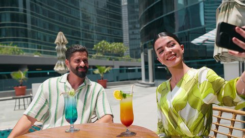زوجان عربيان خليجيان اماراتيين يرتديان الزي الكاجوال يستمتعان بالحديث على طاولة حول المسبح في أحد الفنادق في المملكة العربية السعودية ، الاستمتاع بالمشروبات الصيفية المنعشة, استخدام التقنيات الحديثة ، التقاط صور السيلفي باستخدام الجوال ،توثيق اللحظات التذكارية
