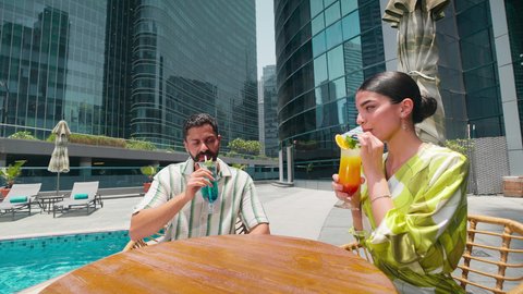 Doing fun recreational activities, enjoying refreshing summer drinks, an Arab Gulf Emirati couple in casual wear enjoying a conversation at a table around the pool in one of the hotels in the Kingdom of Saudi Arabia, luxury chalets and resorts