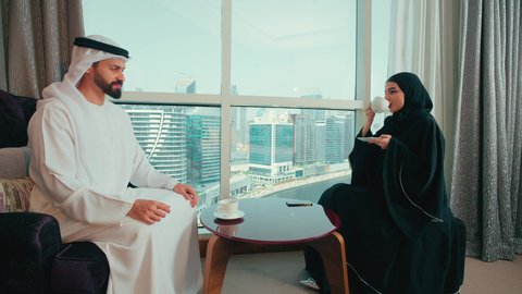 مفهوم الرابطة الزوجية والألفة بين الزوجين, رجل عربي خليجي اماراتية يرتدي الكندورة و الغتره يجلس بجانب النافذة فى المنزل برفقة زوجته ، الاستمتاع بتناول المشروبات ، قضاء وقت ممتع ، أجواء مليئة بالحب