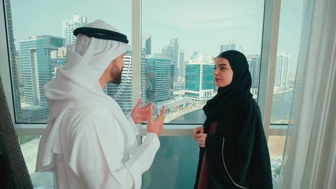 ايماءات السعادة و السرور، مفهوم الترابط الفكري و التفاهم بين الزوجين، تبادل الدردشات و الأحاديث في المنزل ، رجل عربي خليجي اماراتي  يرتدي الكندورة و الغتره يقوم بالاشارة الى شيء ما، سيدة اماراتية محجبة ترتدي العباءة  تتحدث مع زوجها