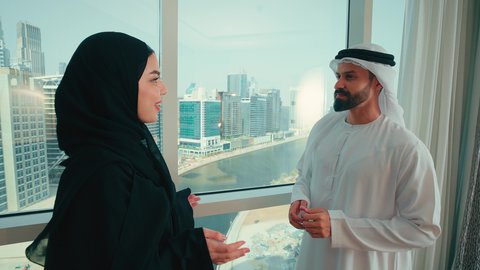 مفهوم الترابط الفكري و التفاهم بين الزوجين، تبادل الدردشات و الأحاديث في المنزل ، رجل عربي خليجي اماراتي  يرتدي الكندورة و الغتره يقوم بالاشارة الى شيء ما، سيدة اماراتية محجبة ترتدي العباءة  تتحدث مع زوجها ، ايماءات السعادة و السرور