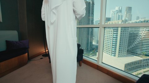 مفهوم الطاقة والإيجابية، قضاء وقت ممتع و هادئ، الحيوية والنشاط عند شرب الكافيين، رجل عربي خليجي اماراتي يرتدي الكندورة و الغتره يجلس على كرسي بجانب النافذة يحمل بيده فنجان من القهوه، الاستمتاع بتناول المشروبات الساخن