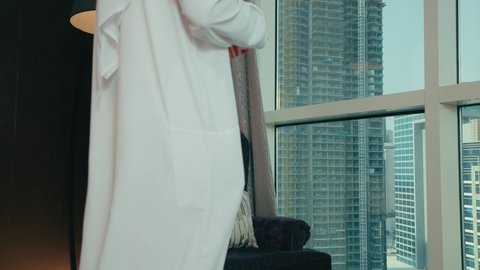 مفهوم الطاقة والإيجابية، قضاء وقت ممتع و هادئ، الحيوية والنشاط عند شرب الكافيين، رجل عربي خليجي اماراتي يرتدي الكندورة و الغتره يجلس على كرسي بجانب النافذة يحمل بيده فنجان من القهوه، الاستمتاع بتناول المشروبات الساخن