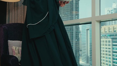 الحيوية والنشاط عند شرب الكافيين، امراة عربيه خليجيه اماراتية مبتسمه ترتدي العباءه السوداء تجلس على كرسي بجانب النافذة تقوم بالاستمتاع بتناول المشروبات الساخن، سيده سعوديه تحمل بيديها فنجان القهوه، قضاء وقت ممتع و هادئ