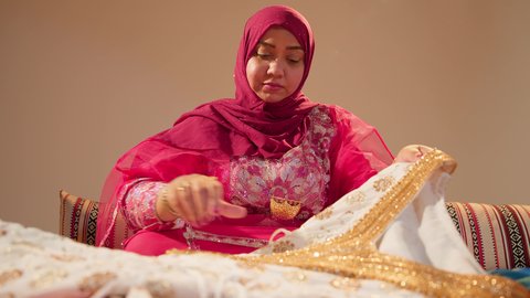 The groom's mother holds in her hands a luxurious jalabiya to present it as a gift to the bride, the rituals of Emirati marriage, the affection and inherited traditions in happy occasions, the traditional folk attire.