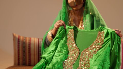 الزي الشعبي التراثي التقليدي، التحضيرات التقليدية قبل تقديم الهدايا للعروس، تصوير مقرب لامراة عربيه خليجيه اماراتية ترتدي العباءة المطرزة تقوم بتحضير الجلابيات الاماراتية للعروس