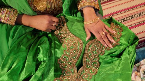 Traditional preparations before presenting gifts to the bride, a close-up shot of the hand of an Emirati Gulf Arab woman wearing an embroidered abaya preparing the Emirati jalabiyas for the bride, the traditional folk heritage attire.
