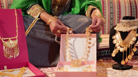 تحضيرات ما قبل الزفاف لتقديم الهدايا والمستلزمات، تصوير مقرب لامراة عربيه خليجيه اماراتية ترتدي العباءة المطرزة تحمل بيديها عقد من الذهب لتقديمه للعروس، ذهب محلي اماراتي وطني، العادات والتقاليد الإماراتية في مراسم الزواج