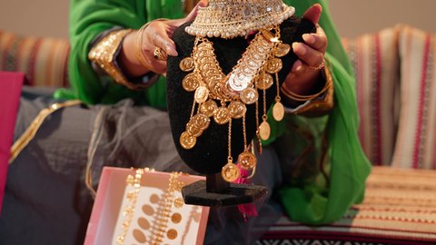 تجهيز الهدايا لتقديمها يوم الزفاف، تصوير مقرب ليد امراة عربيه خليجيه اماراتية ترتدي العباءة المطرزة تحمل بيديها عقد من الذهب لتقديمه للعروس، ذهب محلي اماراتي وطني، العادات والتقاليد الإماراتية في مراسم الزواج