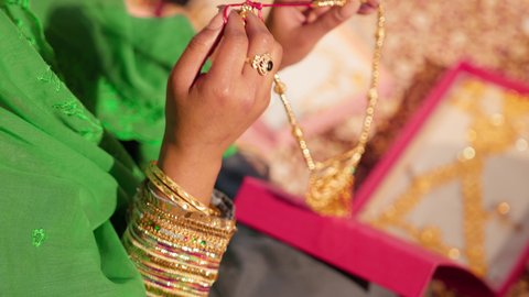 عادات الزواج التراثية في الإمارات العربية المتحدة، التزين بالحلي الذهبية الفاخرة، تقديم الهدايا في المناسبات السعيدة، تصوير مقرب ليد امراة عربيه خليجيه اماراتية تحمل بيديها عقد من الذهب لتقديمه للعروس، ذهب محلي اماراتي وطني