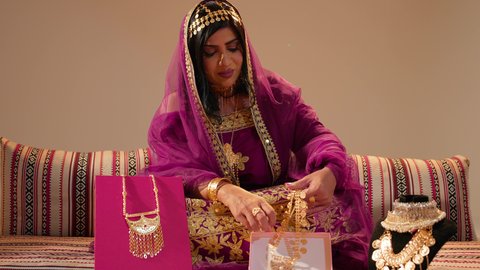تعابير السعاده و السرور، عادات وتقاليد الزواج في الامارات، تقديم الهدايا في المناسبات السعيدة، عروس عربيه خليجيه اماراتية تحمل بيديها عقد من الذهب ، التزين بالحلي الذهبية الفاخرة، ذهب محلي اماراتي وطني