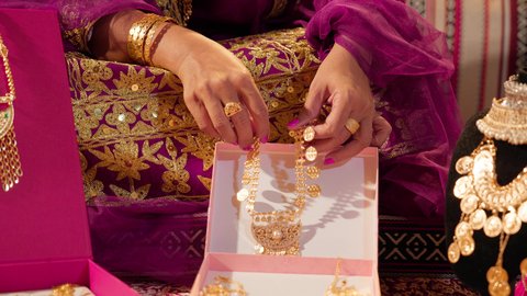 التزين بالحلي الذهبية الفاخرة، عادات وتقاليد الزواج في الامارات، تقديم الهدايا في المناسبات السعيدة، تصوير مقرب ليد عروس عربيه خليجيه اماراتية تحمل بيديها عقد من الذهب ، ذهب محلي اماراتي وطني