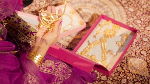 الاستعداد لحفل الزفاف، التزين بالحلي الذهبية الفاخرة، ذهب محلي اماراتي وطني، العادات الإماراتية في تجهيز العروس، تصوير مقرب لأيد عروس عربية خليجيه اماراتية تمسك بيديها عقد ذهبي، ذهب محلي اماراتي وطني