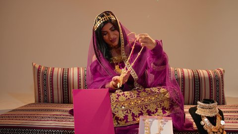 التزين بالحلي الذهبية الفاخرة، العادات الإماراتية في تجهيز العروس، ذهب محلي اماراتي وطني، عروس عربيه خليجيه اماراتية ترتدي العباءة المطرز تمسك بيديها عقد من الذهب ، ايماءات السعادة و السرور