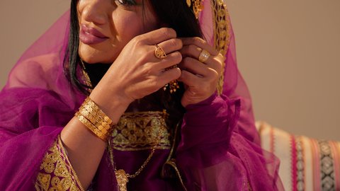 التزين بالحلي الذهبية الفاخرة، ذهب محلي اماراتي وطني، العادات الإماراتية في تجهيز العروس، تصوير مقرب  لعروس عربية خليجيه اماراتية تقوم بارتداء الحلق فى اذنيها