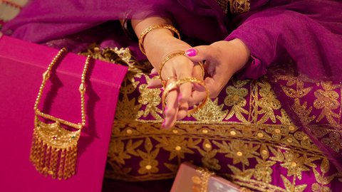 ارتداء الحلي الذهبية الراقية لإبراز الأناقة والفخامة، ذهب محلي اماراتي وطني، العادات الإماراتية في تجهيز العروس، تصوير مقرب ليد عروس عربية خليجيه اماراتية تضع الأساور الذهبية على معصمها