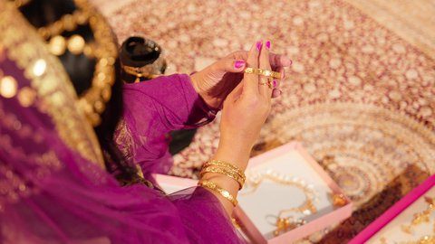 التزين بالمجوهرات الذهبية الفاخرة، العادات الإماراتية في تجهيز العروس، تصوير مقرب من الخلف ليد عروس عربية خليجيه اماراتية تضع الأساور الذهبية على معصمها، ذهب محلي اماراتي وطني