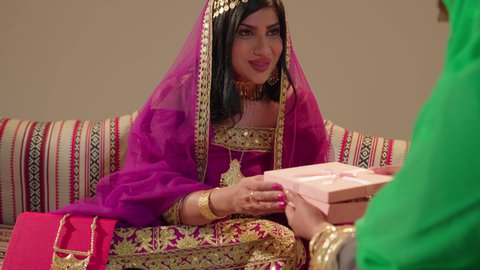 Wedding customs in the UAE, presenting precious gifts to the bride, a close-up shot of an Emirati Gulf Arab woman wearing an embroidered abaya holding a box containing gold jewelry, gestures of astonishment and joy.