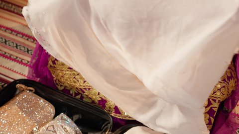 الاحتفال بالعروس في يوم زفافها، عادات وتقاليد الأعراس الإماراتية، تصوير مقرب ليد عروس عربية خليجية إماراتية ترتدي العباءة الملونه تمسك بيديها قطعة قماش بيضاء مطرزة