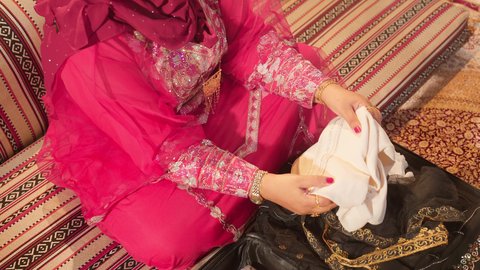 استعدادات ما قبل تقديم الهدايا للعروس، مراسم الاعراس و المناسبات في الامارات ، العطاء والاحتفال بالمناسبات السعيدة،  تصوير مقرب ليد ام العريس ترتدي عباءة مطرزة تمسك بقطعه قماش مطرز