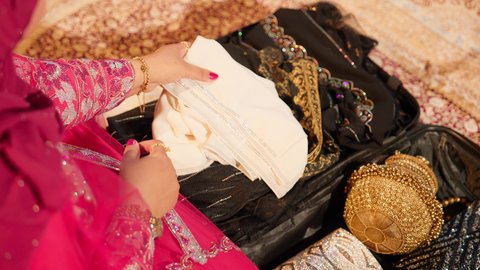 الاستعداد لتقديم الهدايا للعروس، مراسم الاعراس و المناسبات في الامارات ، العطاء والاحتفال بالمناسبات السعيدة،  تصوير مقرب ليد ام العريس ترتدي عباءة مطرزة تمسك بقطعه قماش مطرز