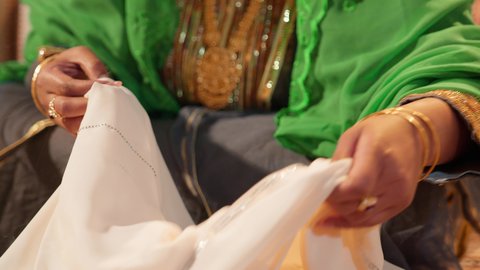 التحضيرات التقليدية قبل تقديم الهدايا للعروس، مراسم الاعراس و المناسبات في الامارات ، العطاء والاحتفال بالمناسبات السعيدة، تصوير مقرب ليد امراة عربية خليجية إماراتية ترتدي عباءة مطرزة تمسك بقطعه قماش مطرز