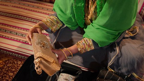 الاستعداد لتقديم الهدايا للعروس، مراسم الزواج في المجتمع الإماراتي، تصوير مقرب ليد امراة عربية خليجية إماراتية ترتدي عباءة مطرزة تحمل حقيبة من الذهب، العطاء والاحتفال بالمناسبات السعيدة