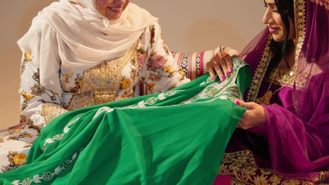 The Emirati rituals in preparing the bride, a close-up shot of the groom's mother gifting the bride an exquisite embroidered jalabiya on the occasion of her wedding, manifestations of joy and celebration during happy occasions.
