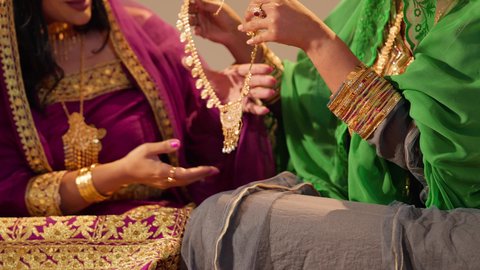 العادات والتقاليد الإماراتية في تقديم الهدايا والمجوهرات، تصوير مقرب لامرأة عربية خليجية إماراتية ترتدي العباءة المطرزة تقدم للعروس عقد ذهبي فاخر، مظاهر الفرح في حفلات الزواج، ذهب محلي اماراتي وطني