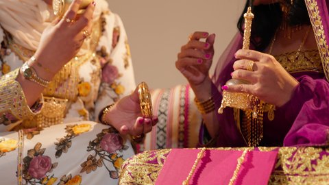 تحضيرات العروس الإماراتية قبل الزفاف، عادات متوارثة تعكس التراث والثقافة الاماراتية في المناسبات السعيدة، تصوير مقرب لام العريس ترتدي العباءة المطرزة تمسك بعلبة بن تقدمها للعروس لتشم رائحتها، ايماءات السعادة و السرور